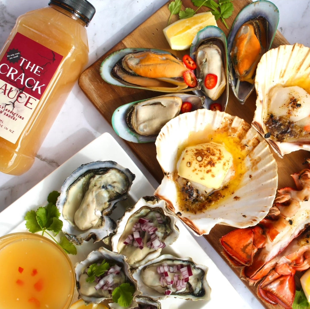 Assorted seafood platter with mussels, scallops, and oysters on a wooden board, accompanied by 'The Crack Sauce' bottle.